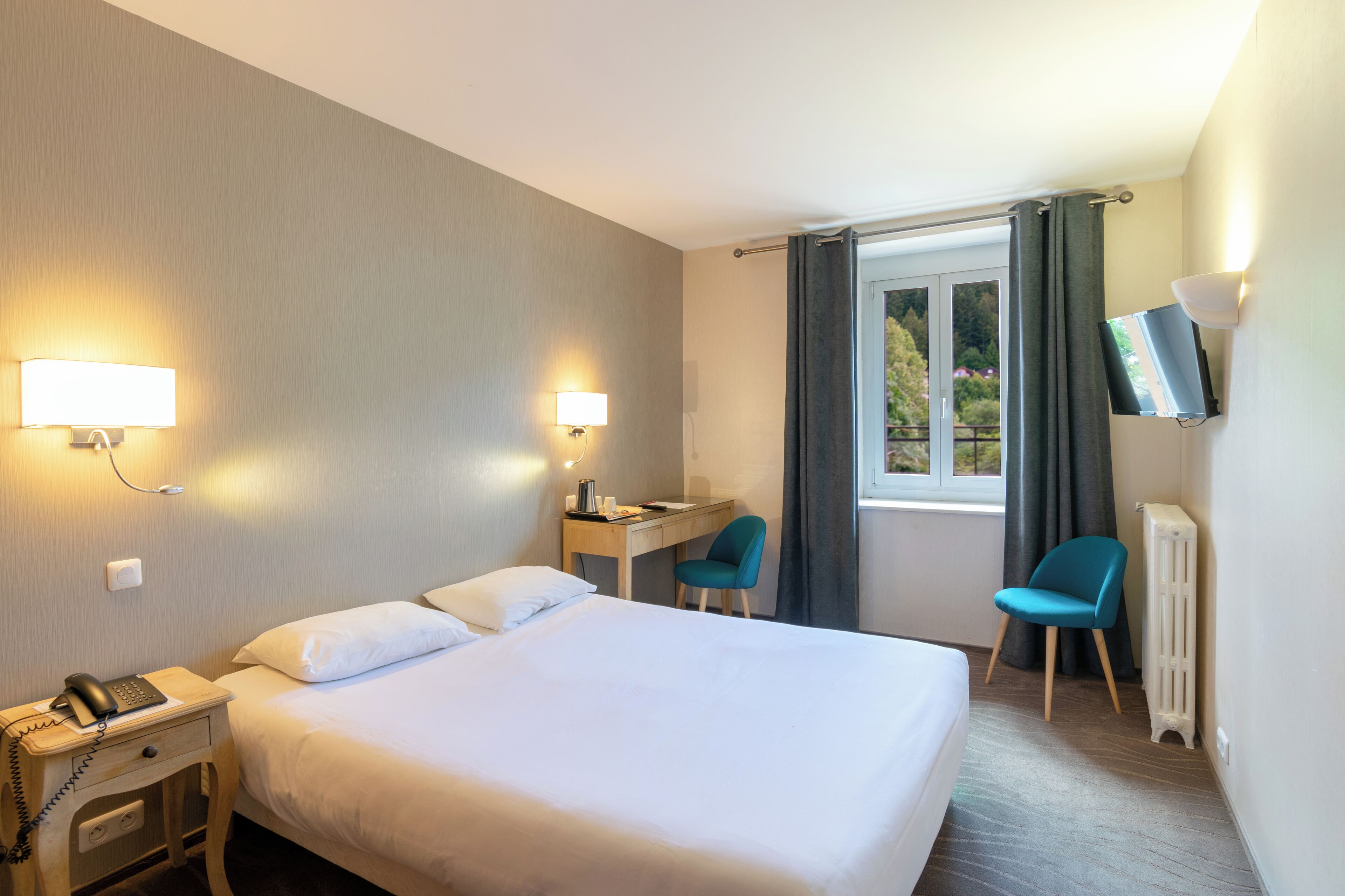 A hotel room with a bed, desk, chair, TV, and window with curtains.