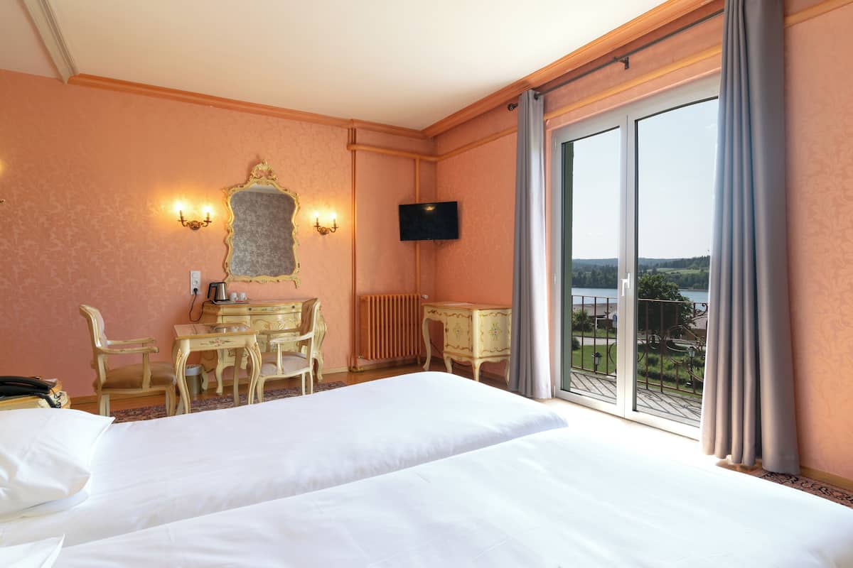 A hotel room with two beds, a desk with a chair, a television, and a large window with a view of the outdoors.