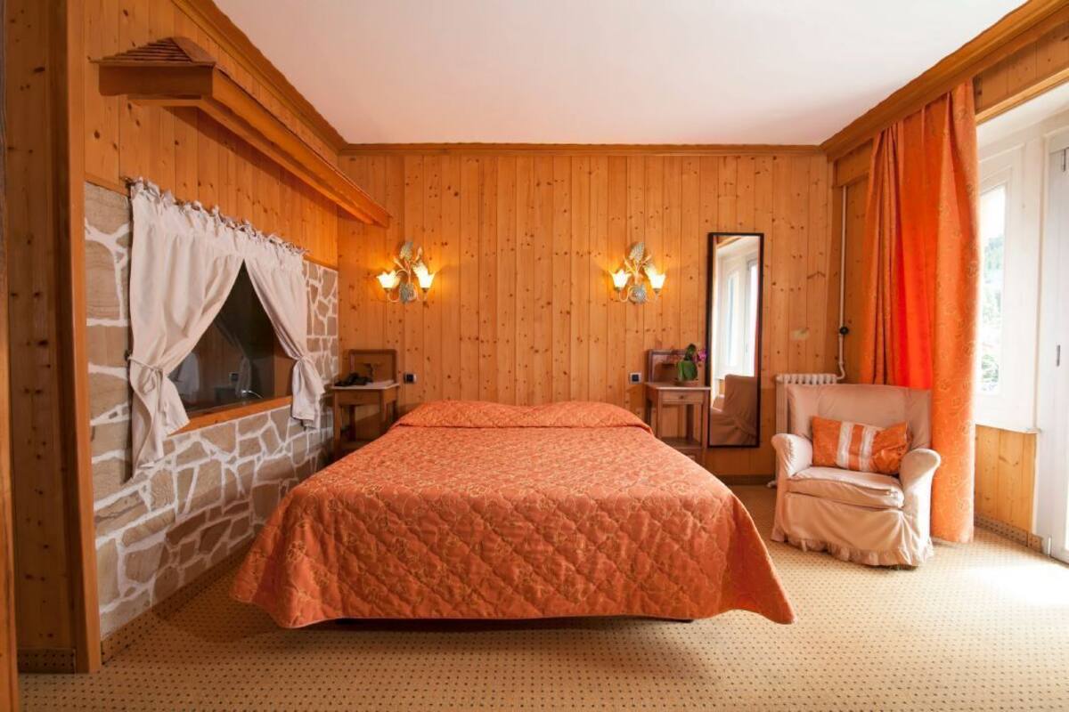 A room with a bed, a stone fireplace, a mirror, a chair, and a window with curtains.
