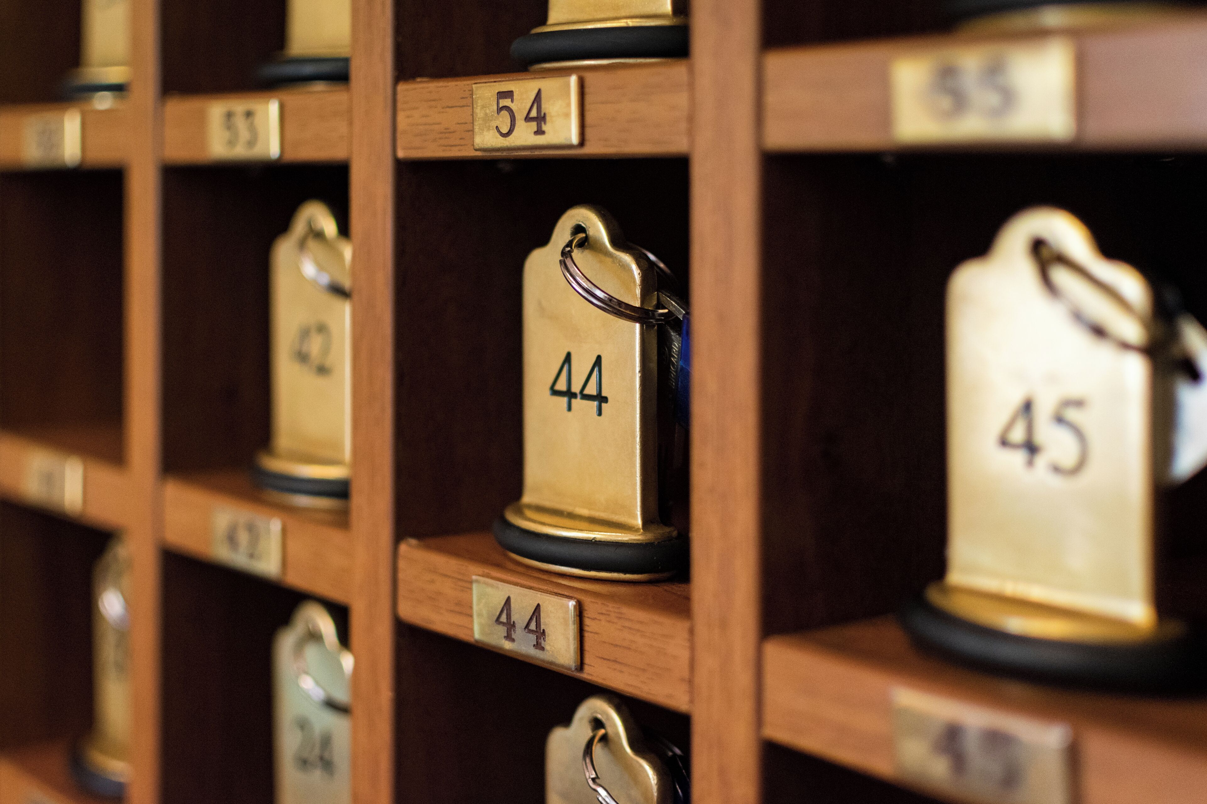A row of wooden shelves with numbered brass keyholders, each labeled with a number from 42 to 55.