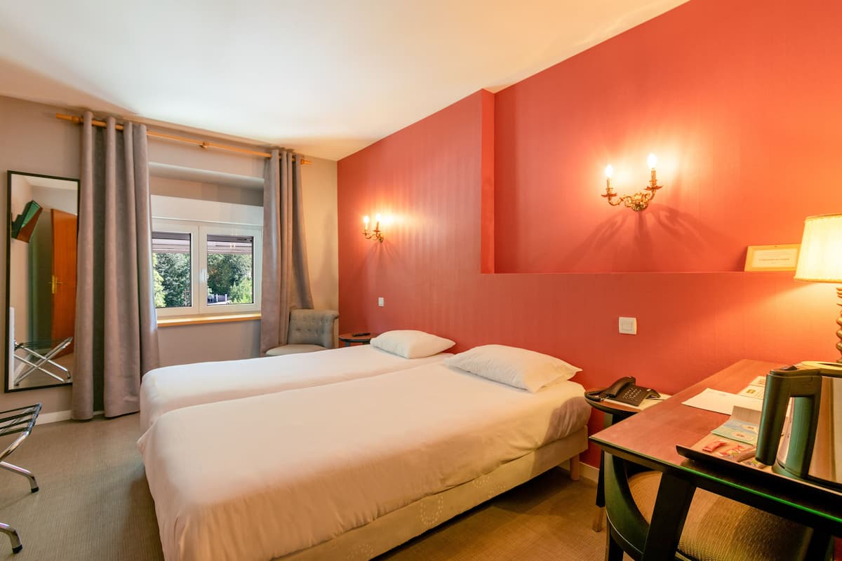 A hotel room with two beds, a desk with a telephone, a chair, and a window with curtains.