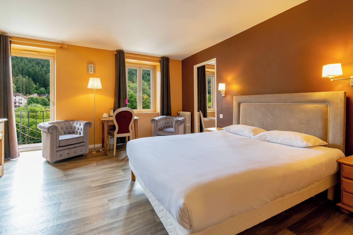A hotel room with a large bed, a desk, two armchairs, and a view of the outdoors.