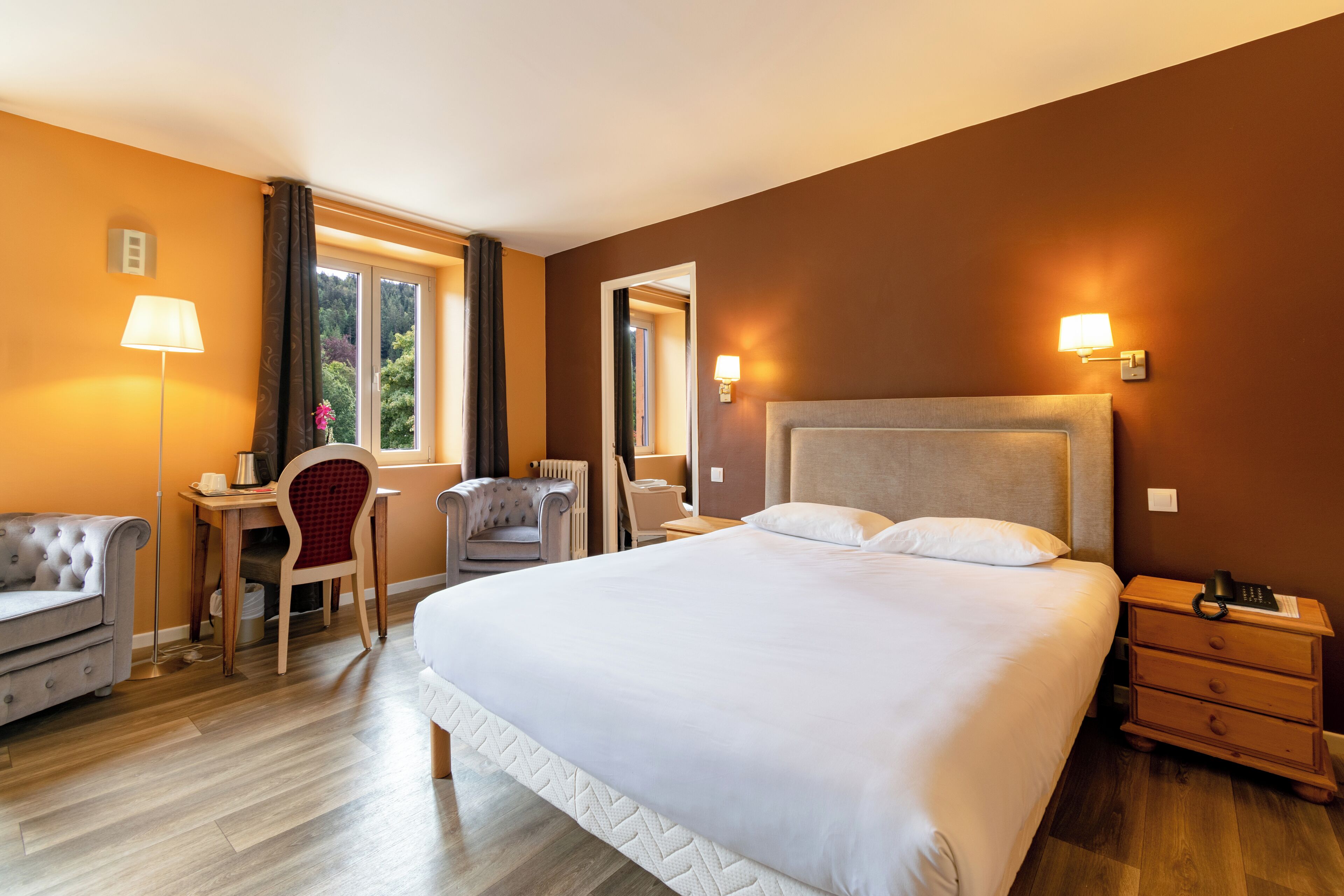 A hotel room with a large bed, a desk with a chair, a lamp, and a nightstand.
