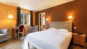 A hotel room with a large bed, a desk with a chair, a lamp, and a nightstand.