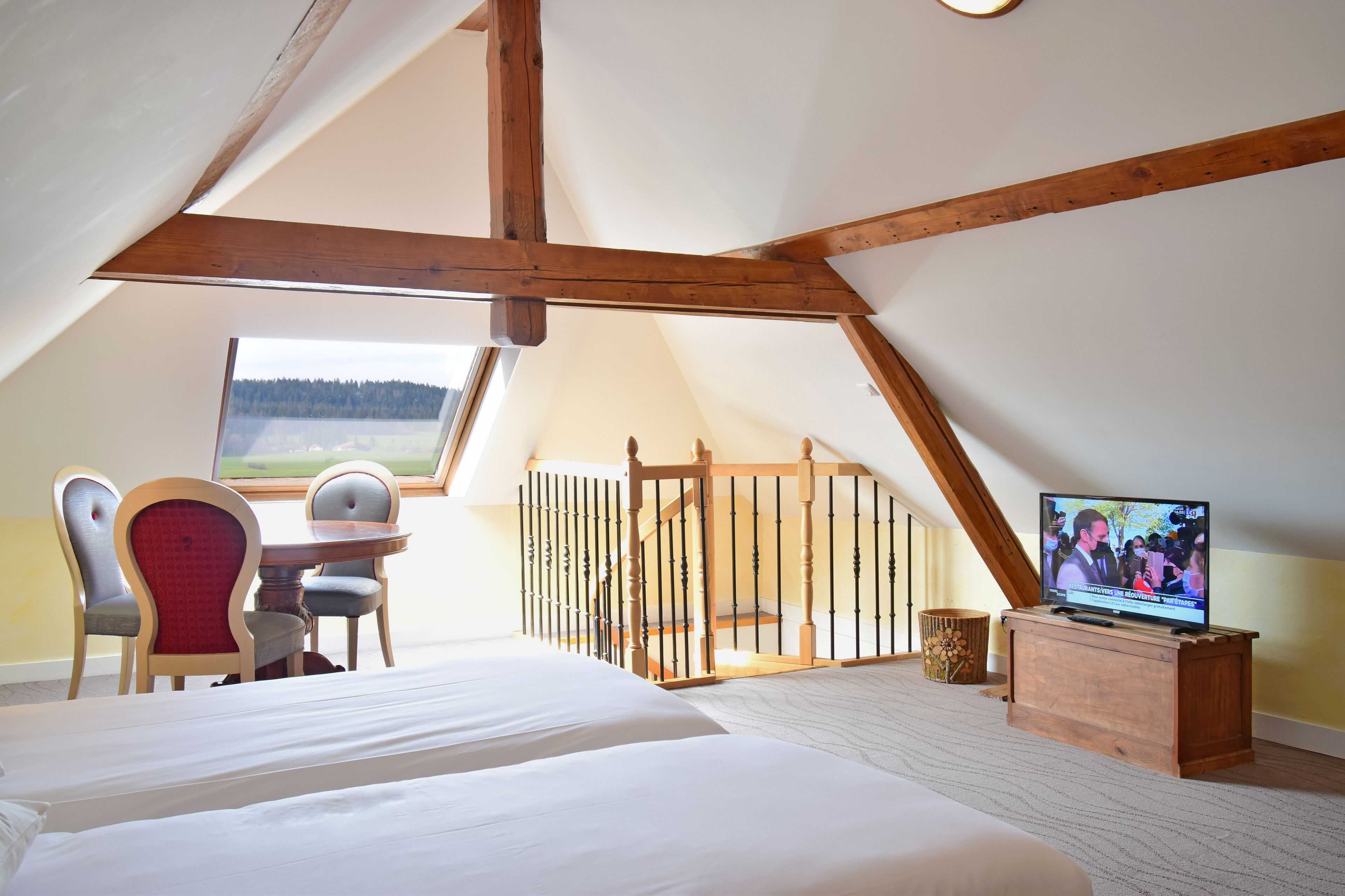 Un dormitorio con una cama grande, un televisor, un escritorio con una silla y una ventana que da a un bosque.