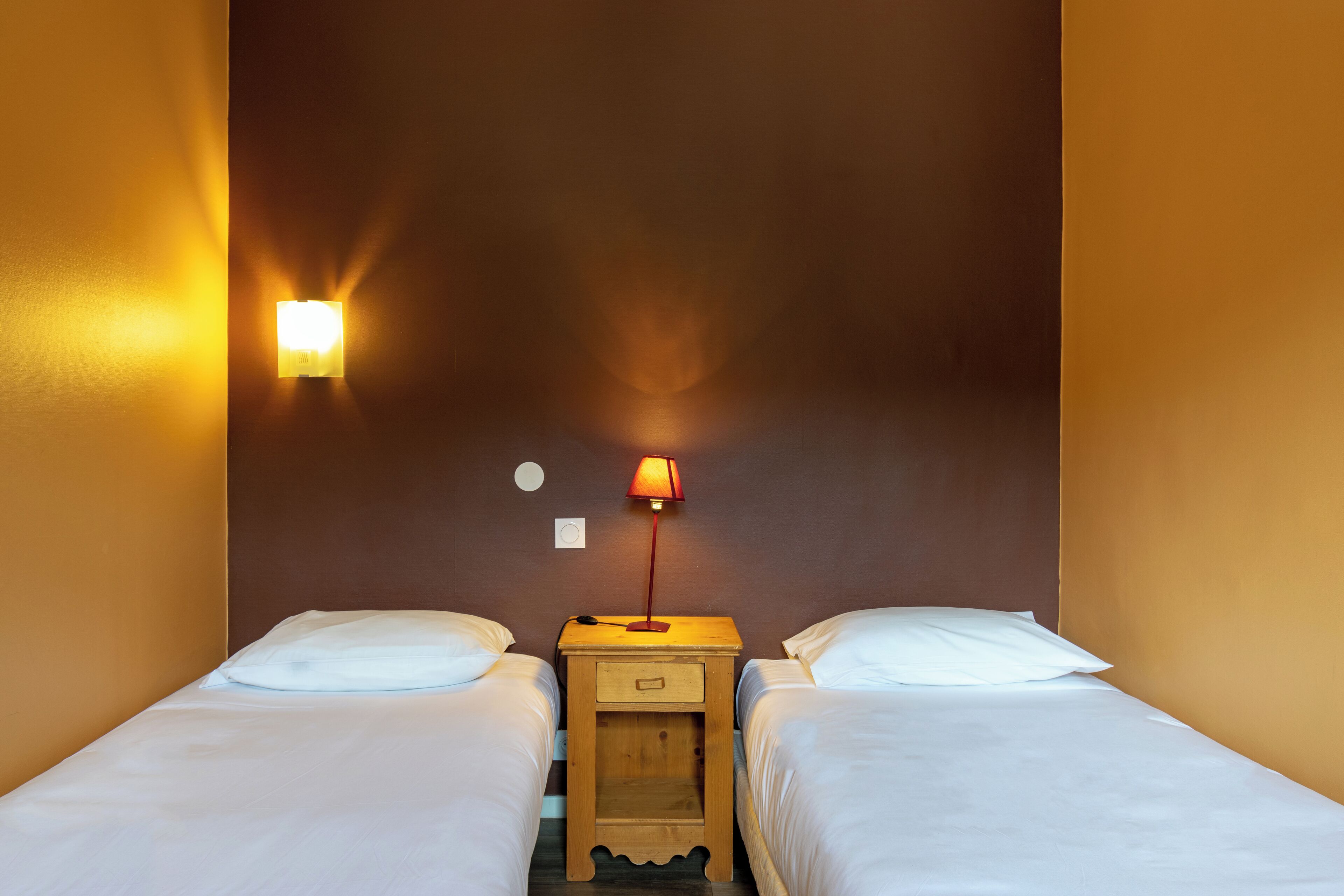 Una habitación de hotel con dos camas, una mesita de noche con lámpara e iluminación en la pared.
