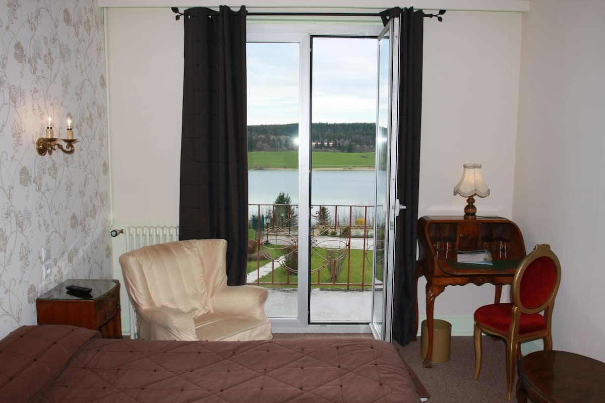 A bedroom with a bed, a chair, a desk, and a view of a green landscape through a large window.