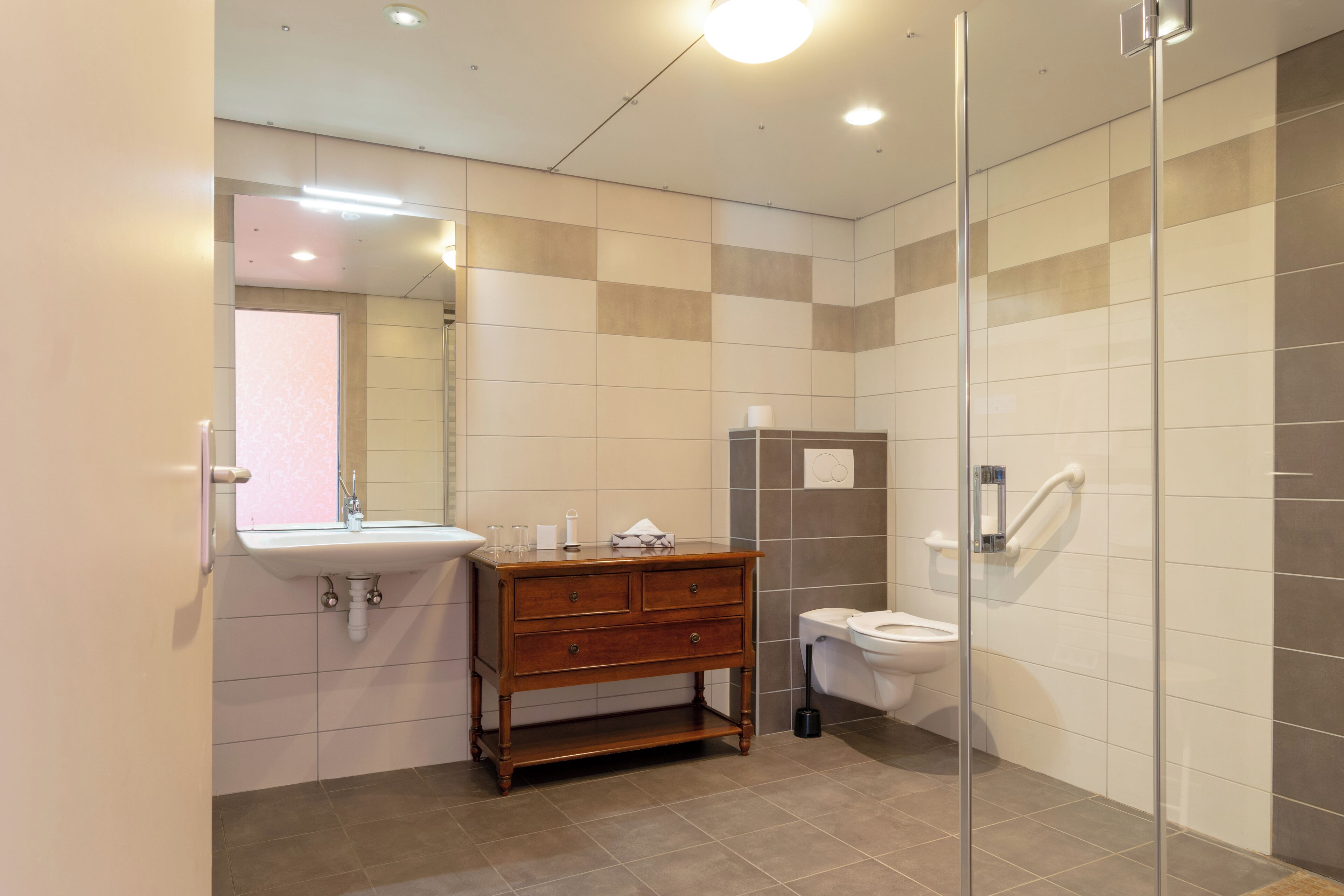 A modern bathroom with a wooden vanity, a sink, a toilet, and a glass shower enclosure.