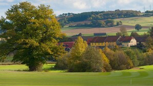 A rural landscape with a golf course, a large tree, and a building with a red roof.