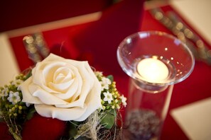 Una rosa blanca en un florero de vidrio con una vela en su interior, sobre una superficie roja.
