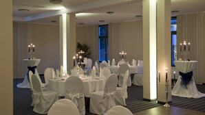 A banquet hall with round tables set for a formal event, white chairs with bows, and tall candelabras with candles.
