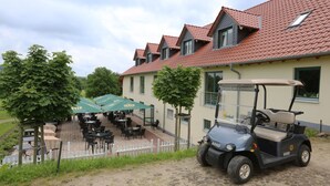 A golf cart parked in front of a building with outdoor seating and a sign reading "Golfpark am Löwenhof".