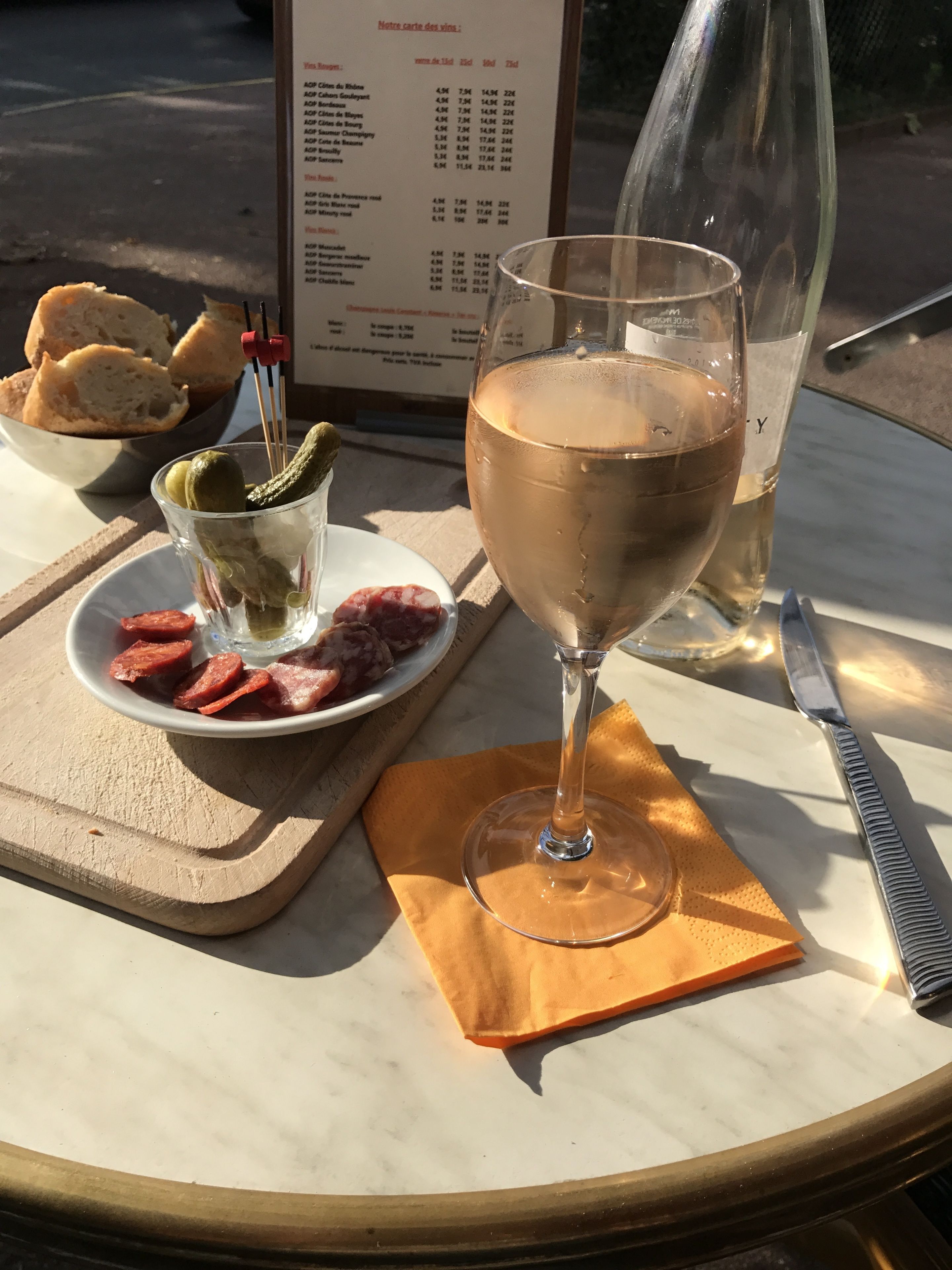 Una mesa con un menú, una copa de vino, un plato de comida y un cuchillo.