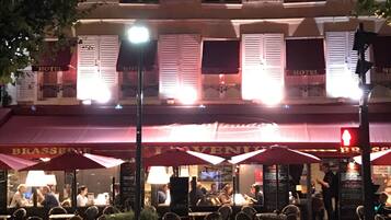 A hotel with a red awning, outdoor seating, and a street lamp.