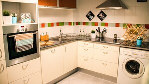 A modern kitchen with stainless steel appliances, a built-in oven, a washing machine, and a variety of utensils and appliances on the countertops.