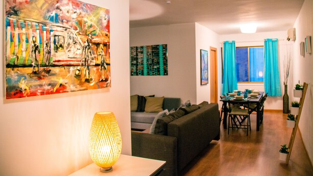 A living room with a sofa, a table with chairs, a painting, and a lamp.
