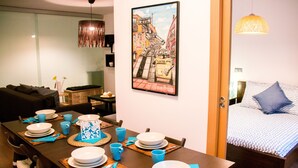 A dining area with a table set for four, a bed with a blue pillow, and a cityscape painting on the wall.