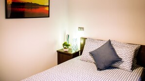 A neatly made bed with patterned bedding, a wall-mounted lamp, and a framed picture of a sunset over water.