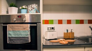 A kitchen with a stainless steel oven, a toaster, and a sink. There are two potted plants on the shelf above the oven.