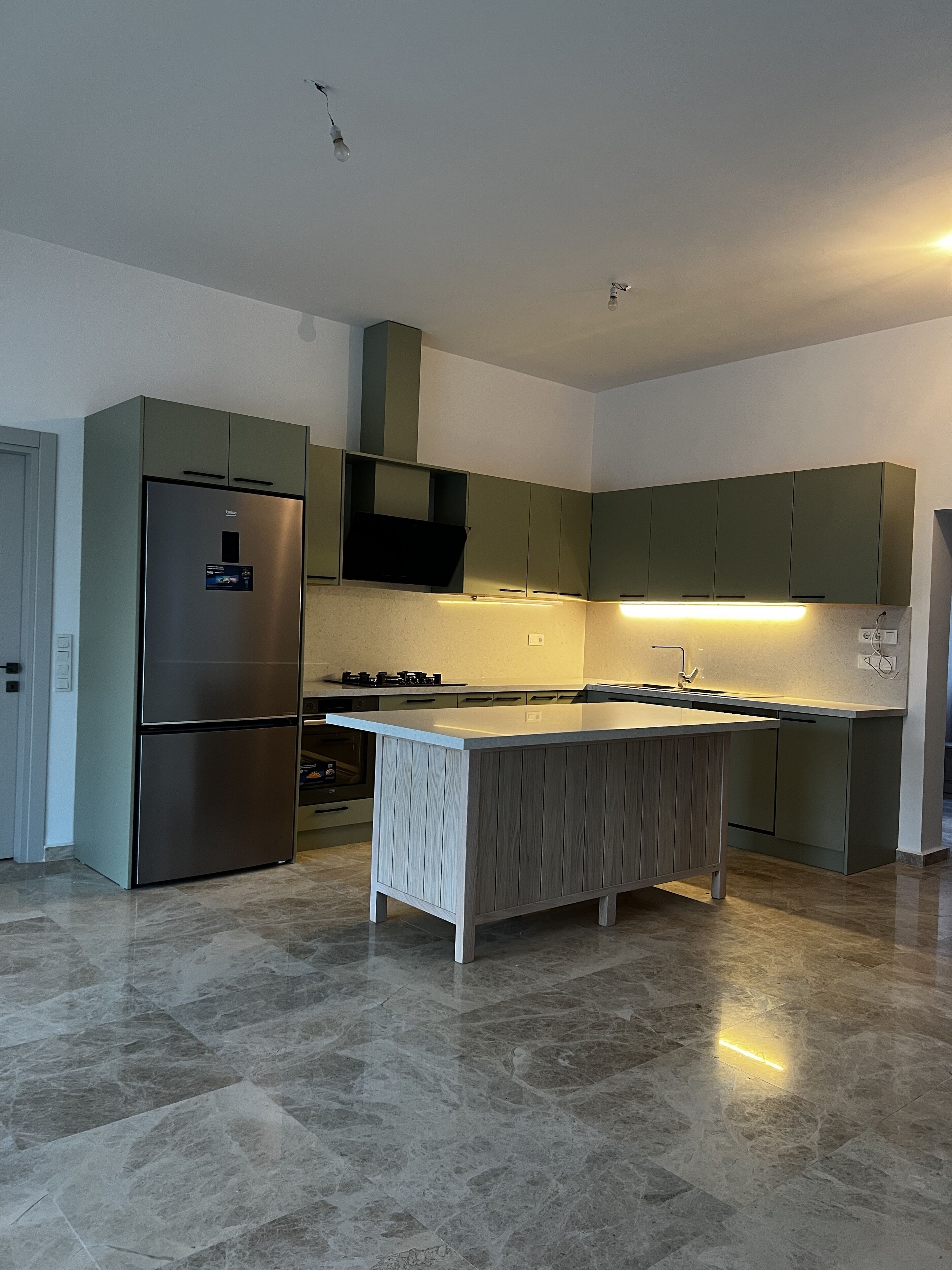 Una cocina moderna con una isla integrada, electrodomésticos de acero inoxidable y armarios color verde.