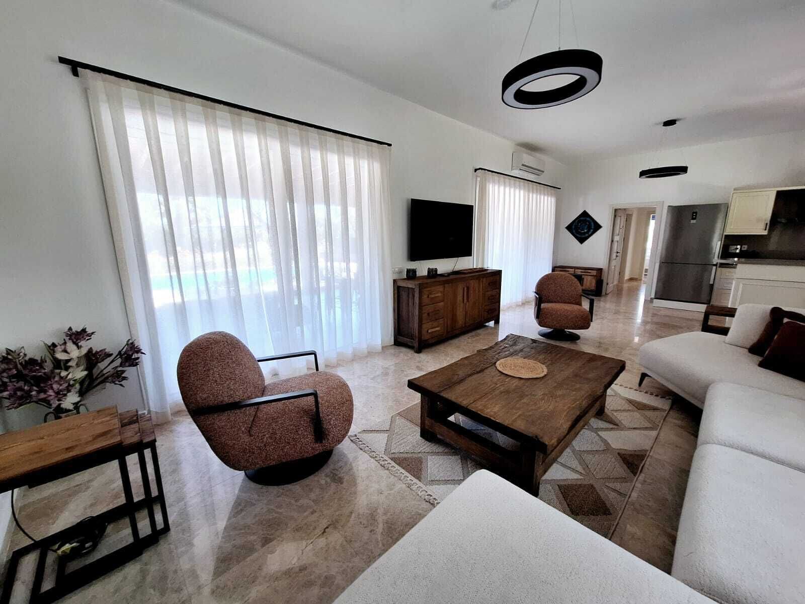 Una sala de estar moderna con un sofá, dos sillones, una mesa de centro y un televisor.