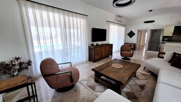 Una sala de estar moderna con un sofá, dos sillones, una mesa de centro y un televisor.