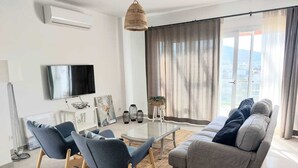 Una sala de estar moderna con un sofá, sillas, una mesa de centro de vidrio y un televisor.