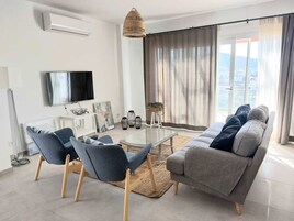 Uma sala de estar moderna com sofá, cadeiras, mesa de centro de vidro e televisão.