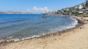 A coastal beach with a pier extending into the sea, surrounded by residential buildings.