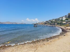 Uma praia costeira com um cais que se estende até o mar, rodeada por edifícios residenciais.