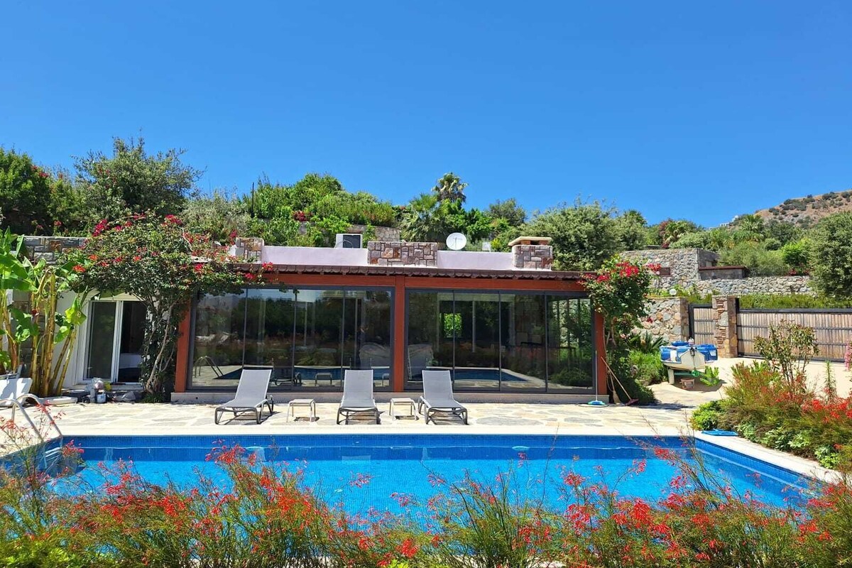 Un espace piscine extérieur moderne, doté de chaises longues, d’un patio fermé par des baies vitrées et d’un mur en pierre.
