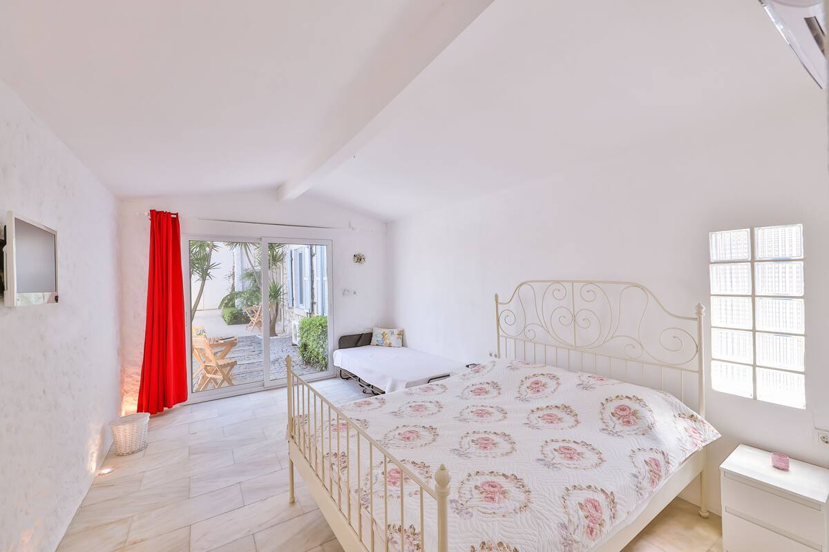 A bedroom with a bed, a window, a door, and a view of the outside.