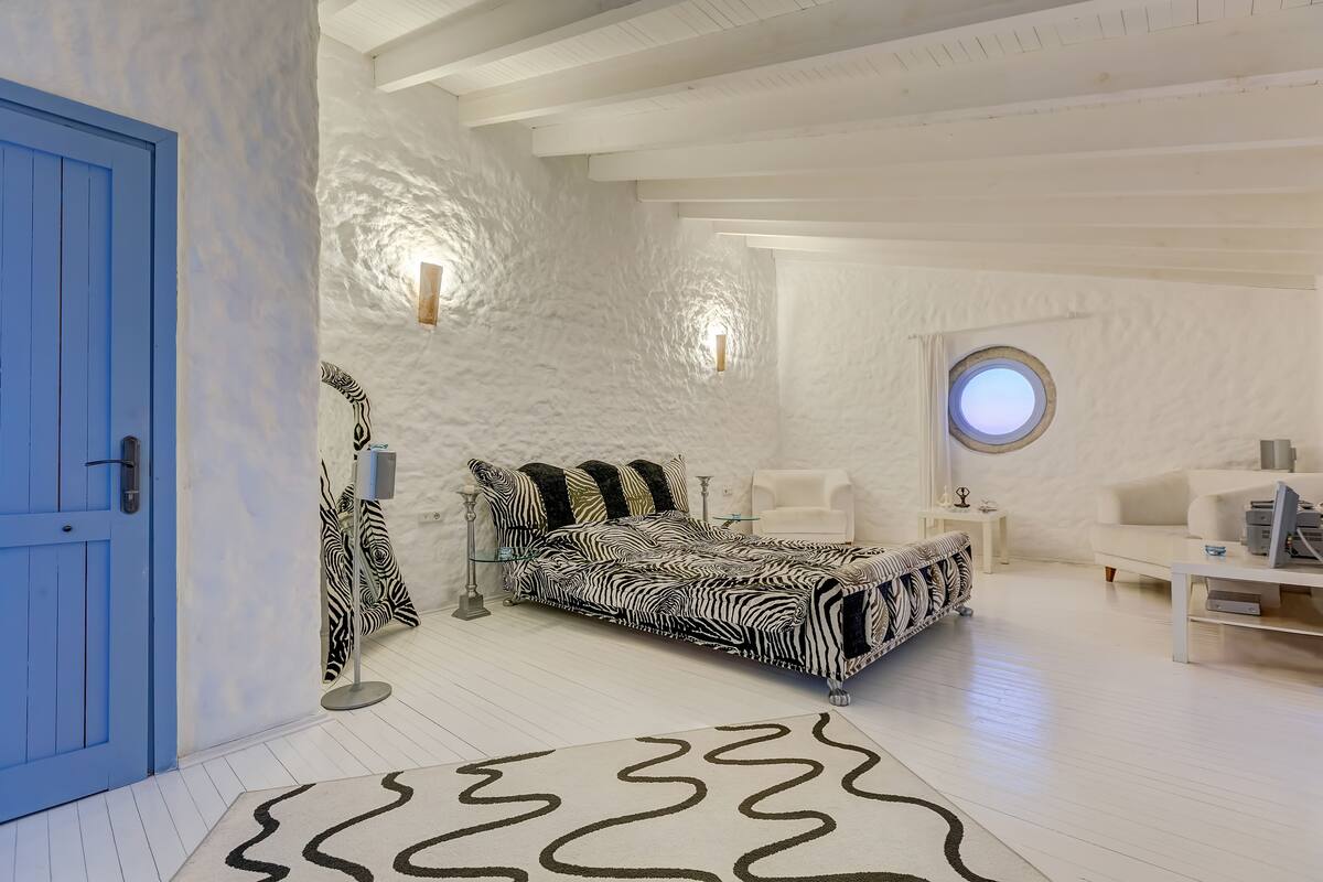 A bedroom with a zebra-patterned bed, a blue door, and a round window.