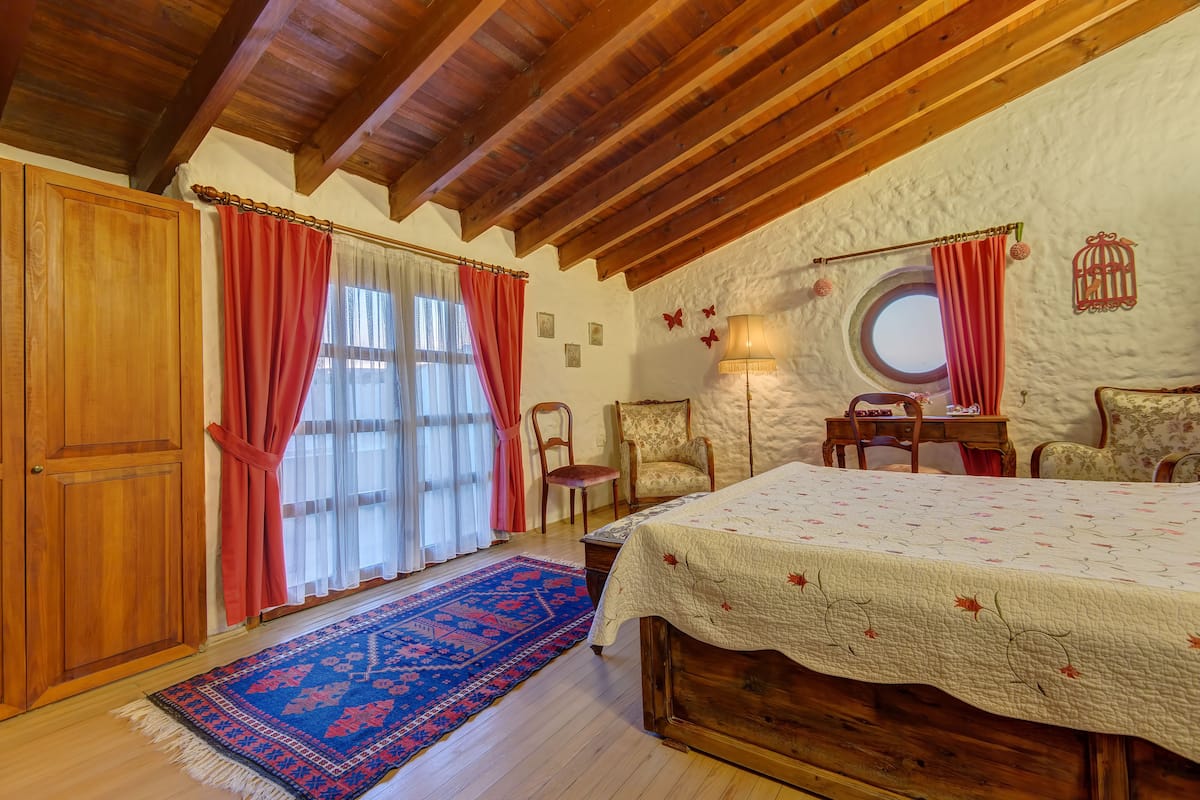A bedroom with a wooden bed, a red and white striped curtain, a round window, and a wooden ceiling.