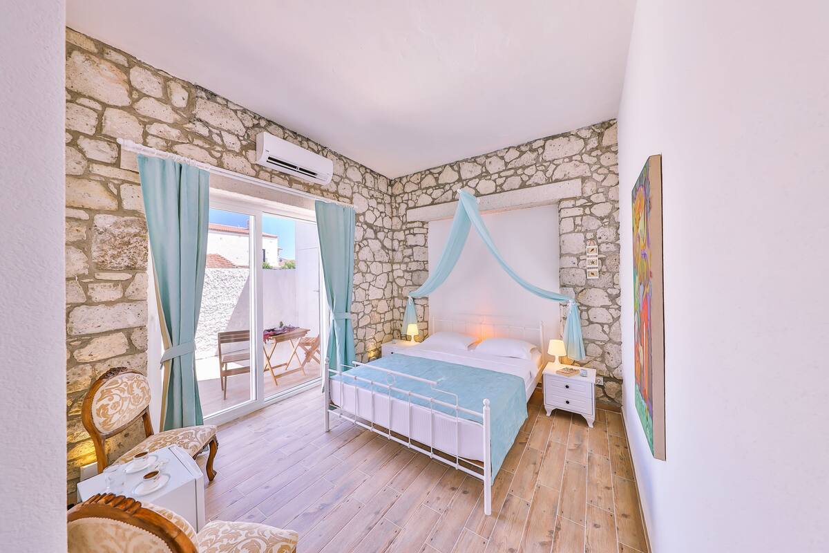 A bedroom with a stone wall, a bed with a canopy, a nightstand, and a chair.