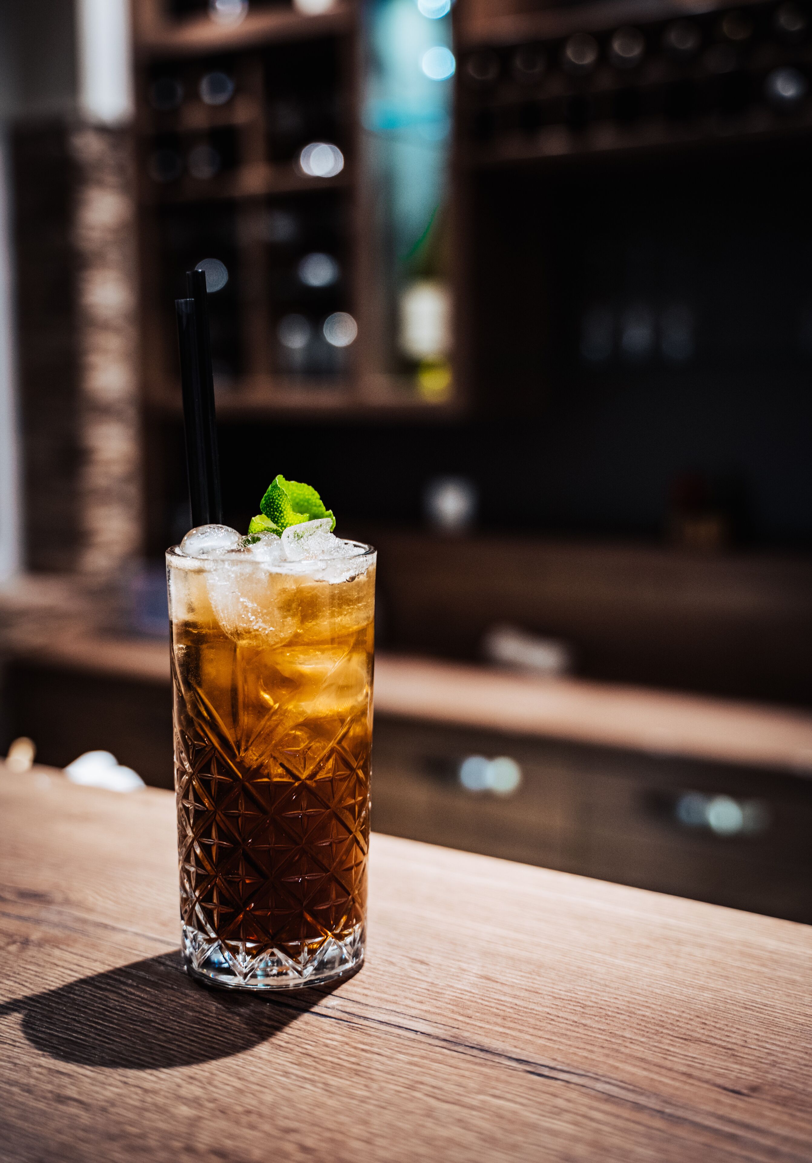Un grand verre avec une paille noire et une feuille de menthe en guise de décoration, posé sur une surface en bois.