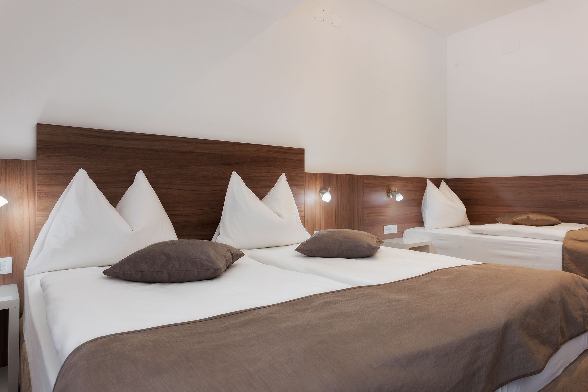 A hotel room with two beds, each with white bedding and brown throw blankets.