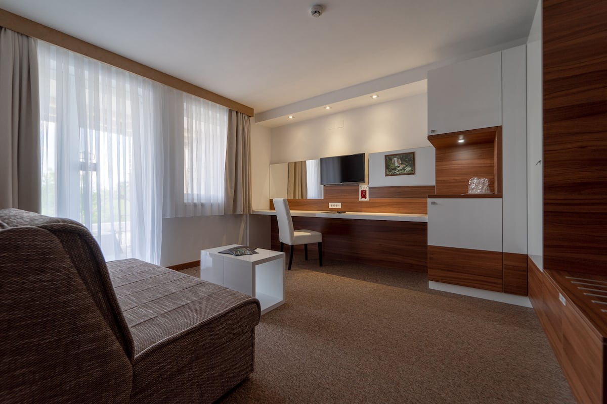 A modern hotel room with a large bed, a desk, a chair, and a TV.