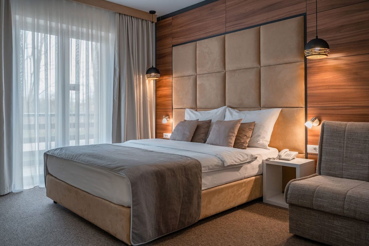 A modern hotel room with a large bed, a nightstand, a chair, and a wooden accent wall.