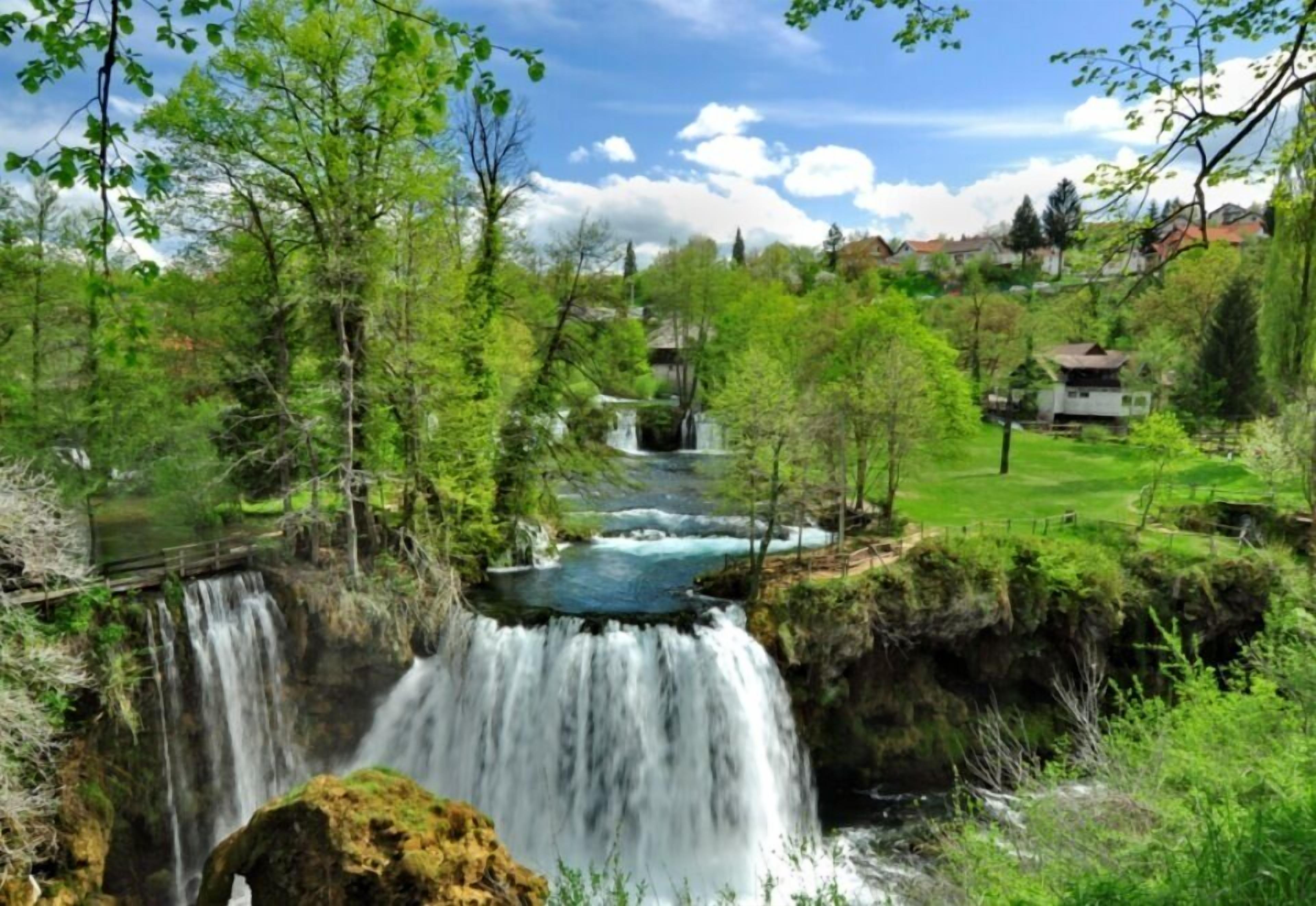 A waterfall surrounded by lush greenery and a clear sky.