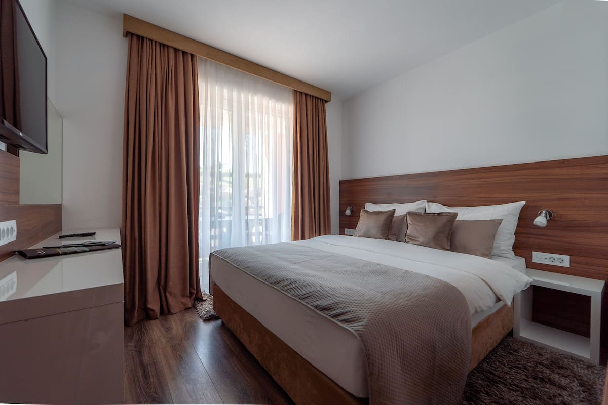 A modern hotel room with a large bed, wooden headboard, a flat-screen TV, and a desk with a remote control.