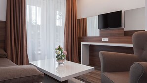 Una habitación de hotel moderna con un ventanal grande, un televisor de pantalla plana en la pared, un sofá, una mesa de centro con un jarrón de flores y una pared decorativa de madera.
