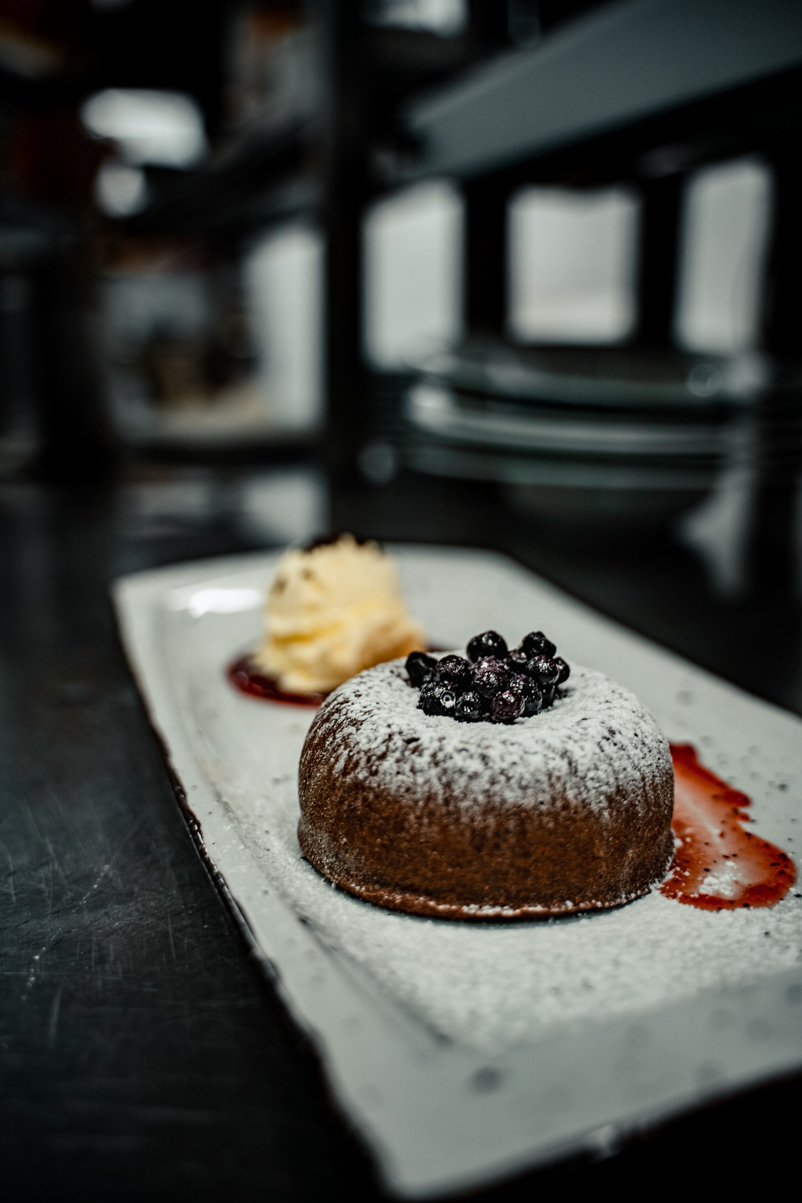 A dessert on a white plate with powdered sugar and blueberries on top, accompanied by a scoop of ice cream and a berry sauce.