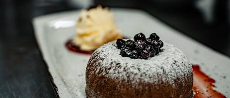 A dessert on a white plate with powdered sugar and blueberries on top, accompanied by a scoop of ice cream and a berry sauce.