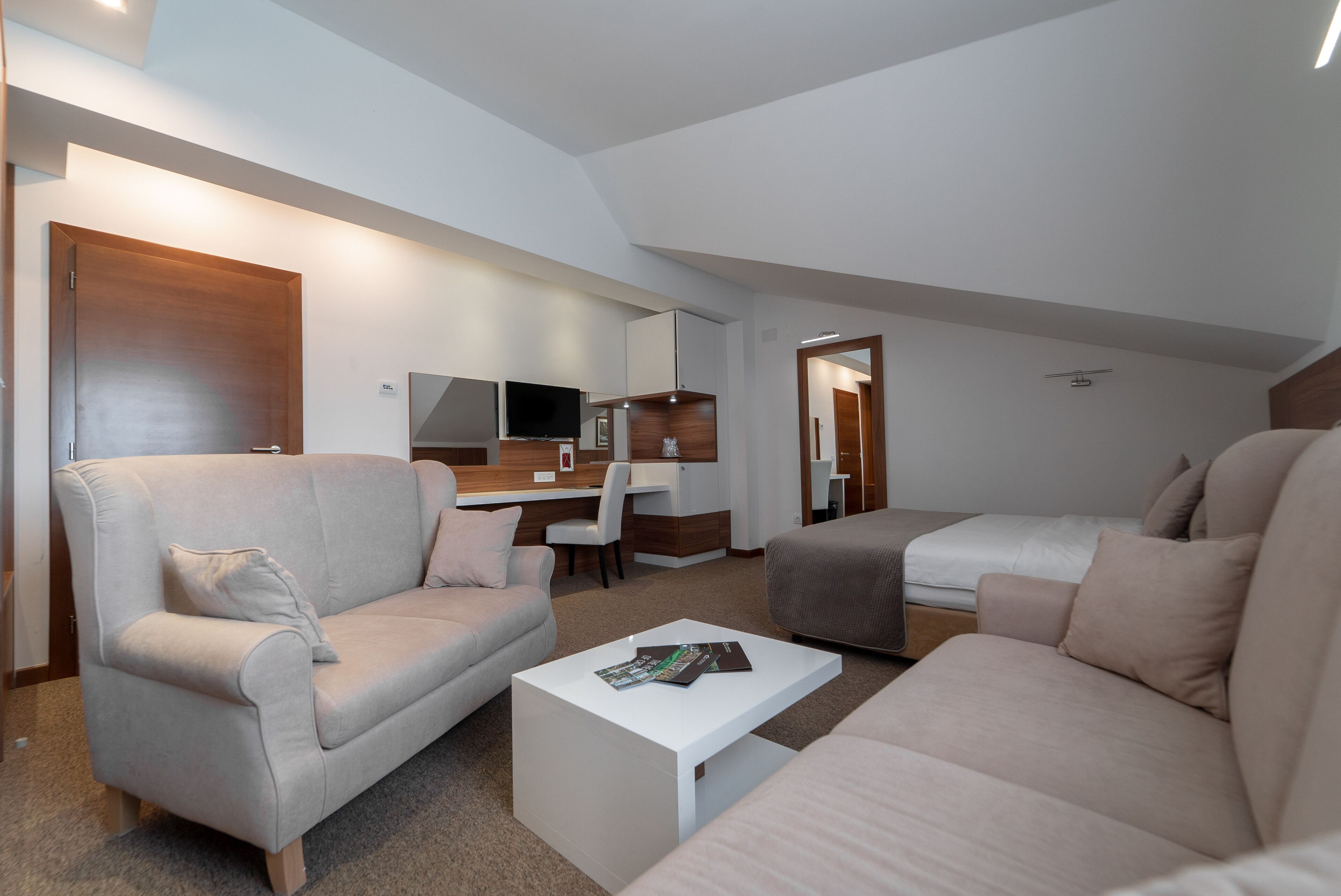 Ein modernes, helles Zimmer mit einer Couch, einem Couchtisch, einem Schreibtisch und einem Bett.