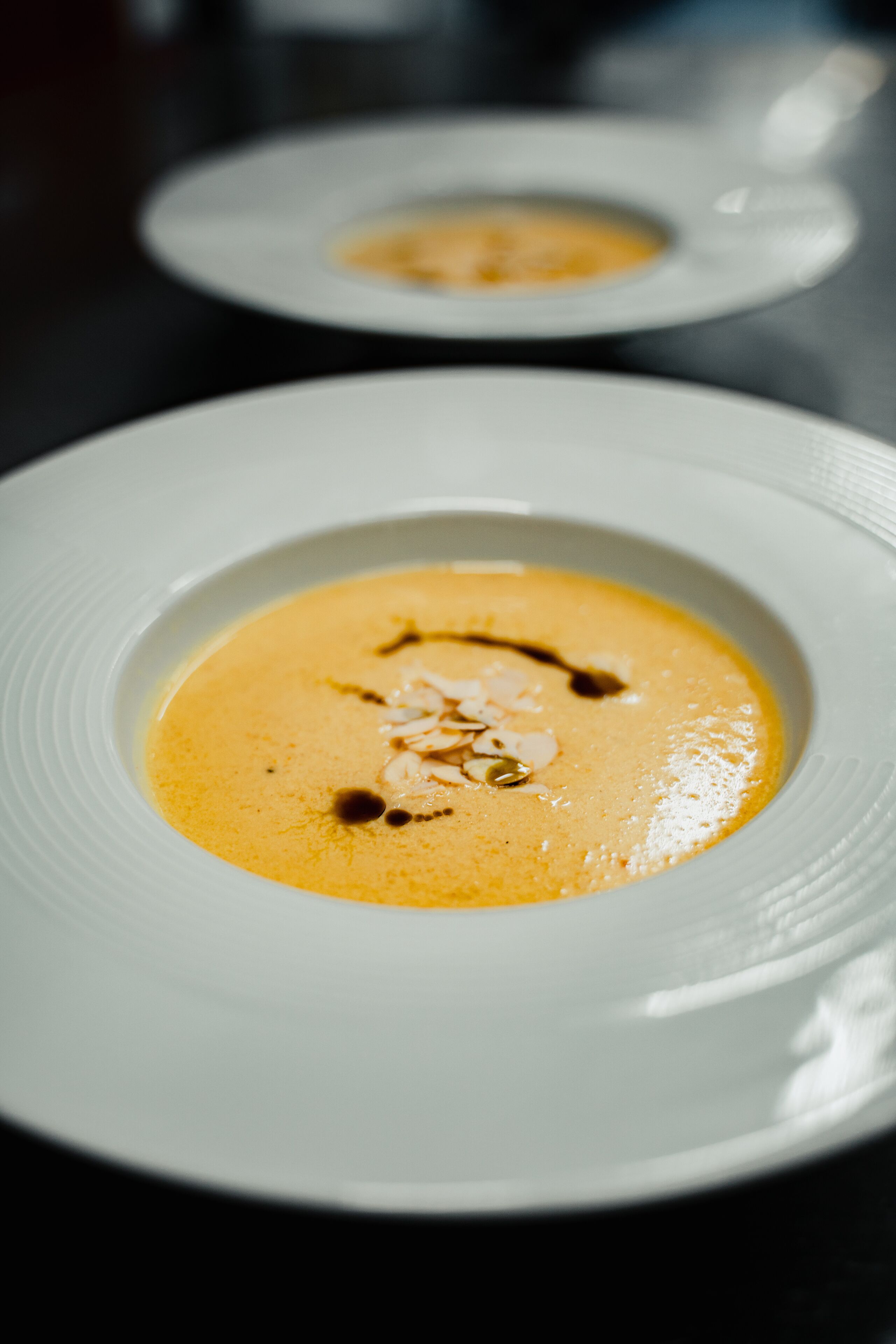 A close-up of a creamy soup with a drizzle of sauce and almond slices on a white plate.