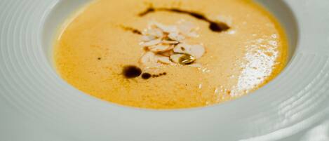 A close-up of a creamy soup with a drizzle of sauce and almond slices on a white plate.