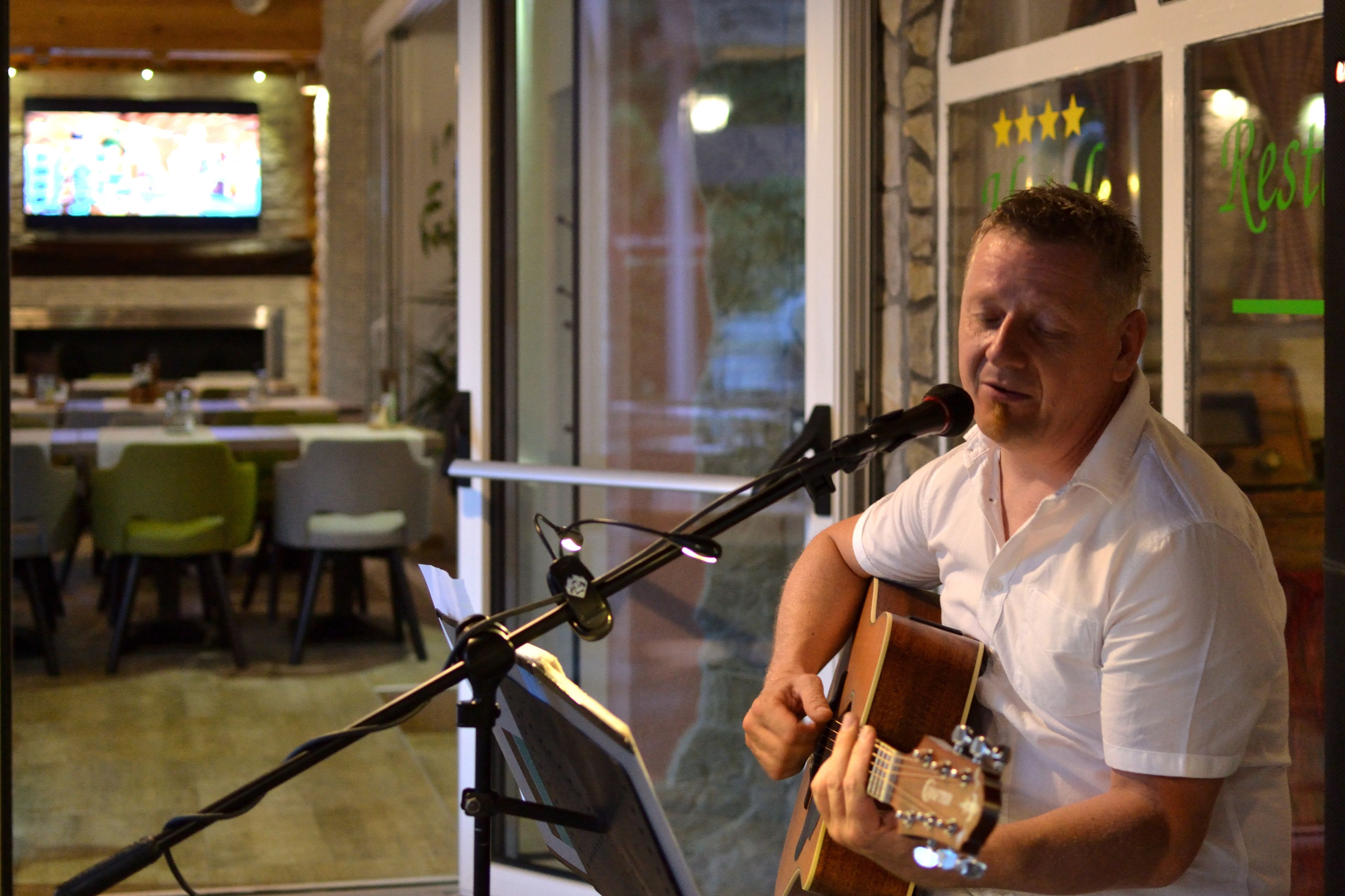 A man playing guitar at a microphone stand in a restaurant with a TV in the background.