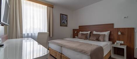 A hotel room with a large bed, a desk, a chair, a nightstand with a phone, and a painting on the wall.