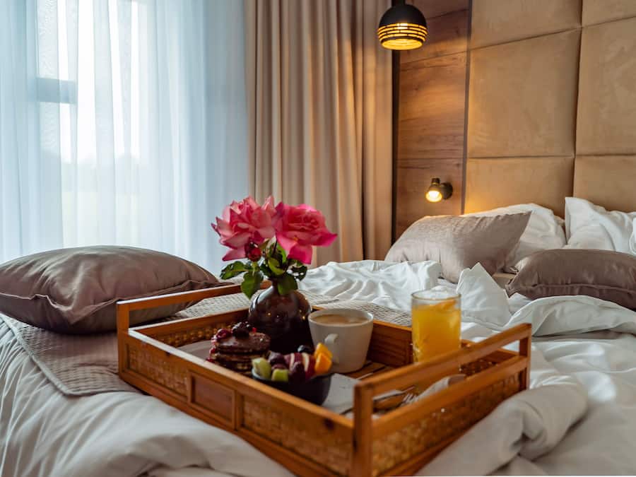 Cama arrumada com uma bandeja de itens de café da manhã, incluindo uma xícara de café, um copo de suco de laranja e uma seleção de doces.